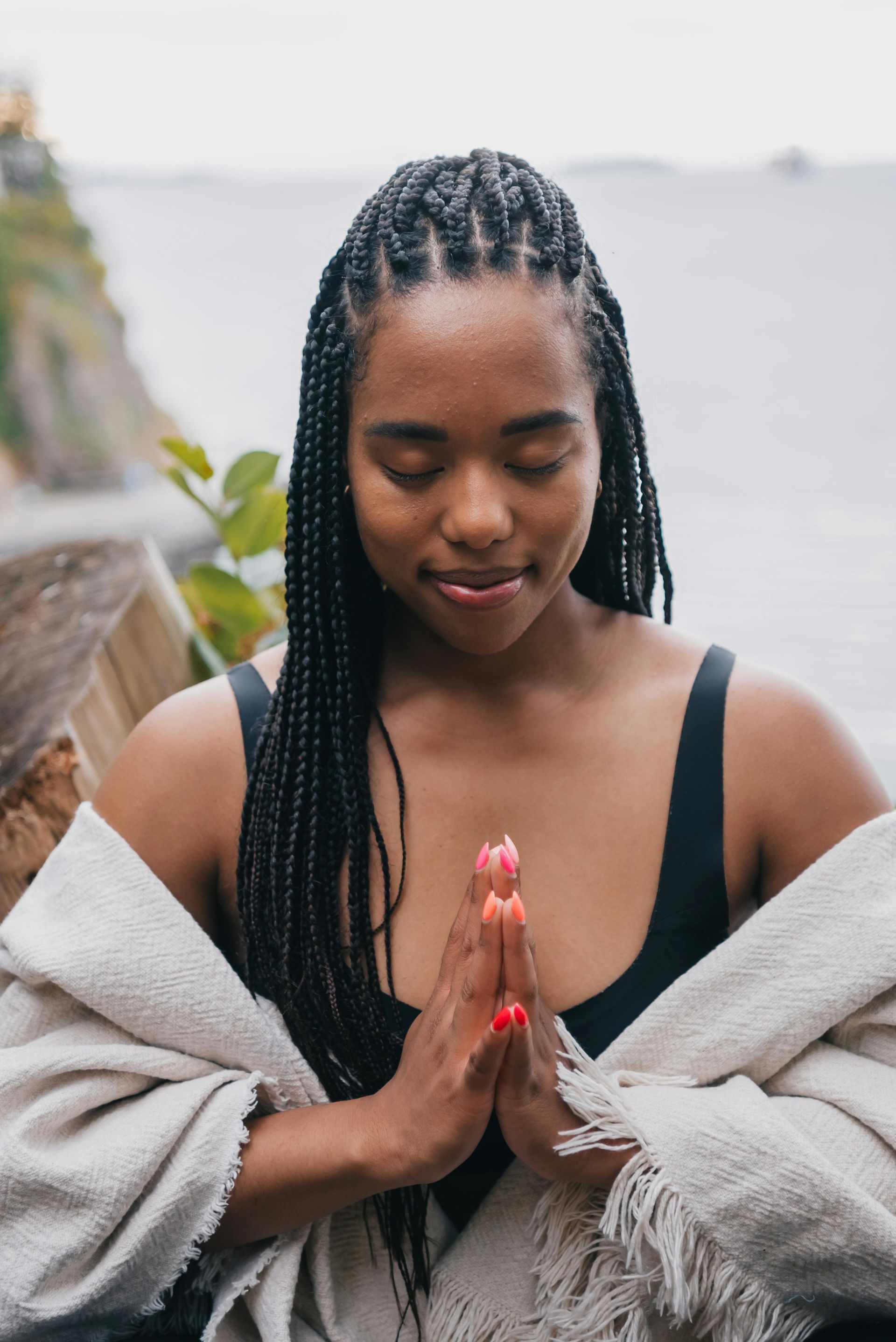 A woman is wrapped in a blanket and meditating with her eyes closed.