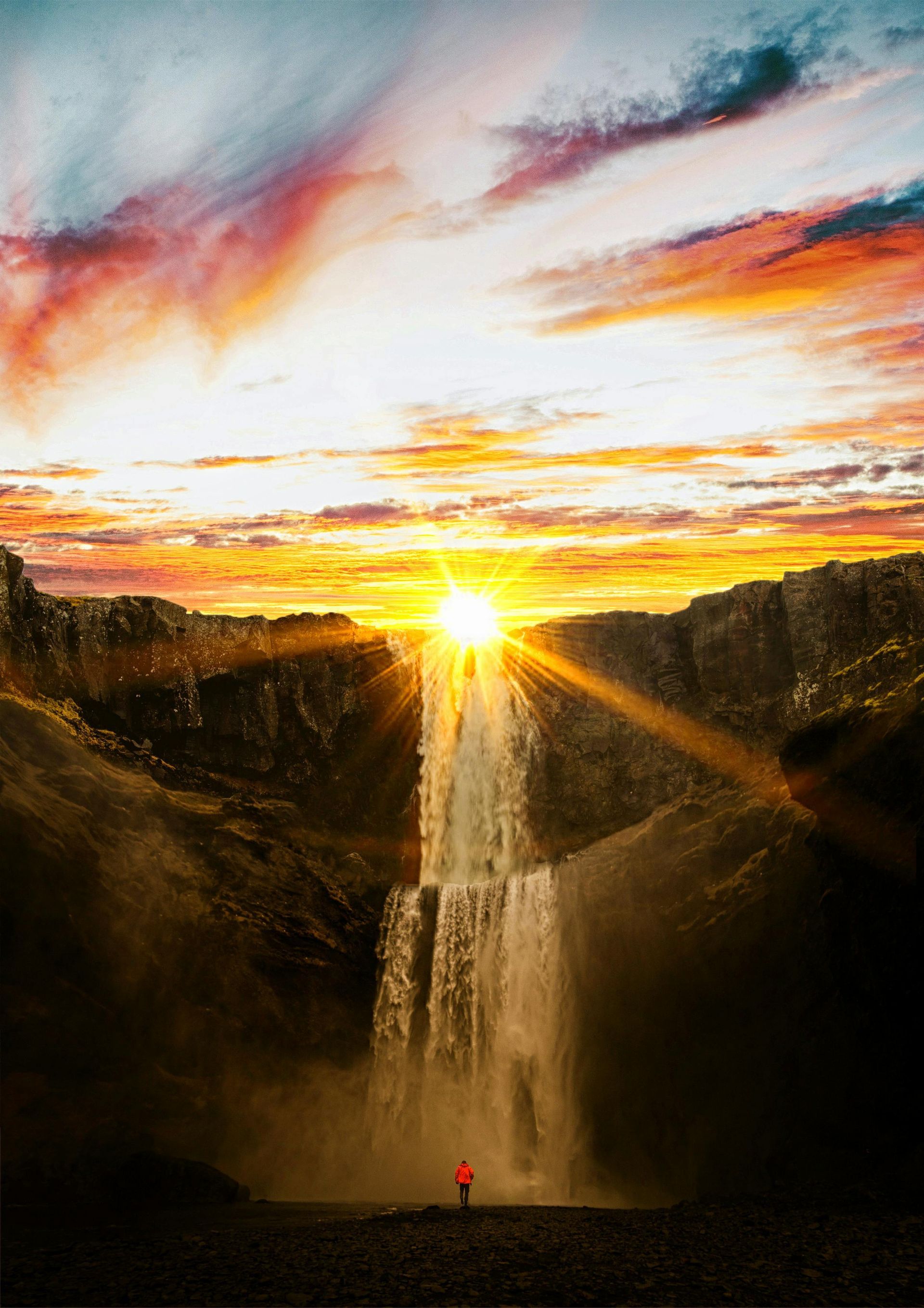 A person is standing in front of a waterfall at sunset.