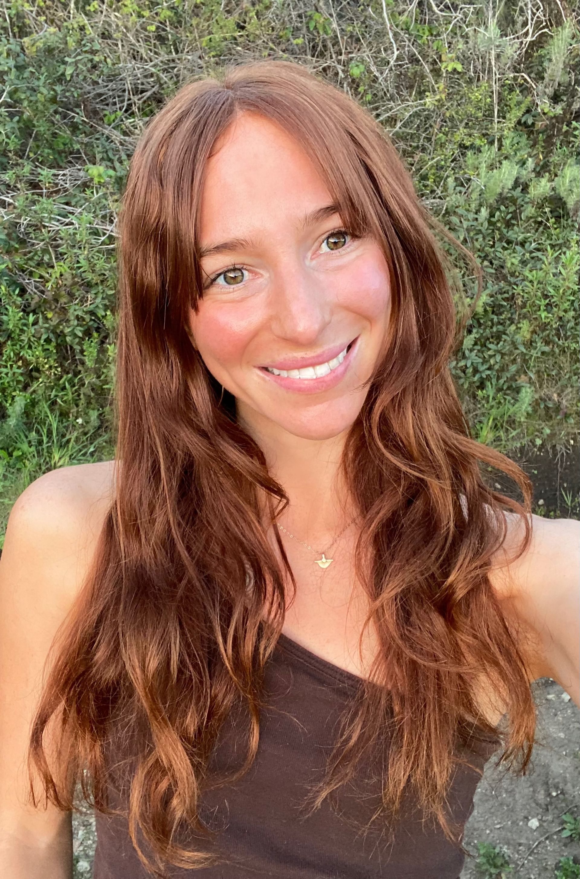 A woman wearing a green shirt and a gold necklace is smiling for the camera.