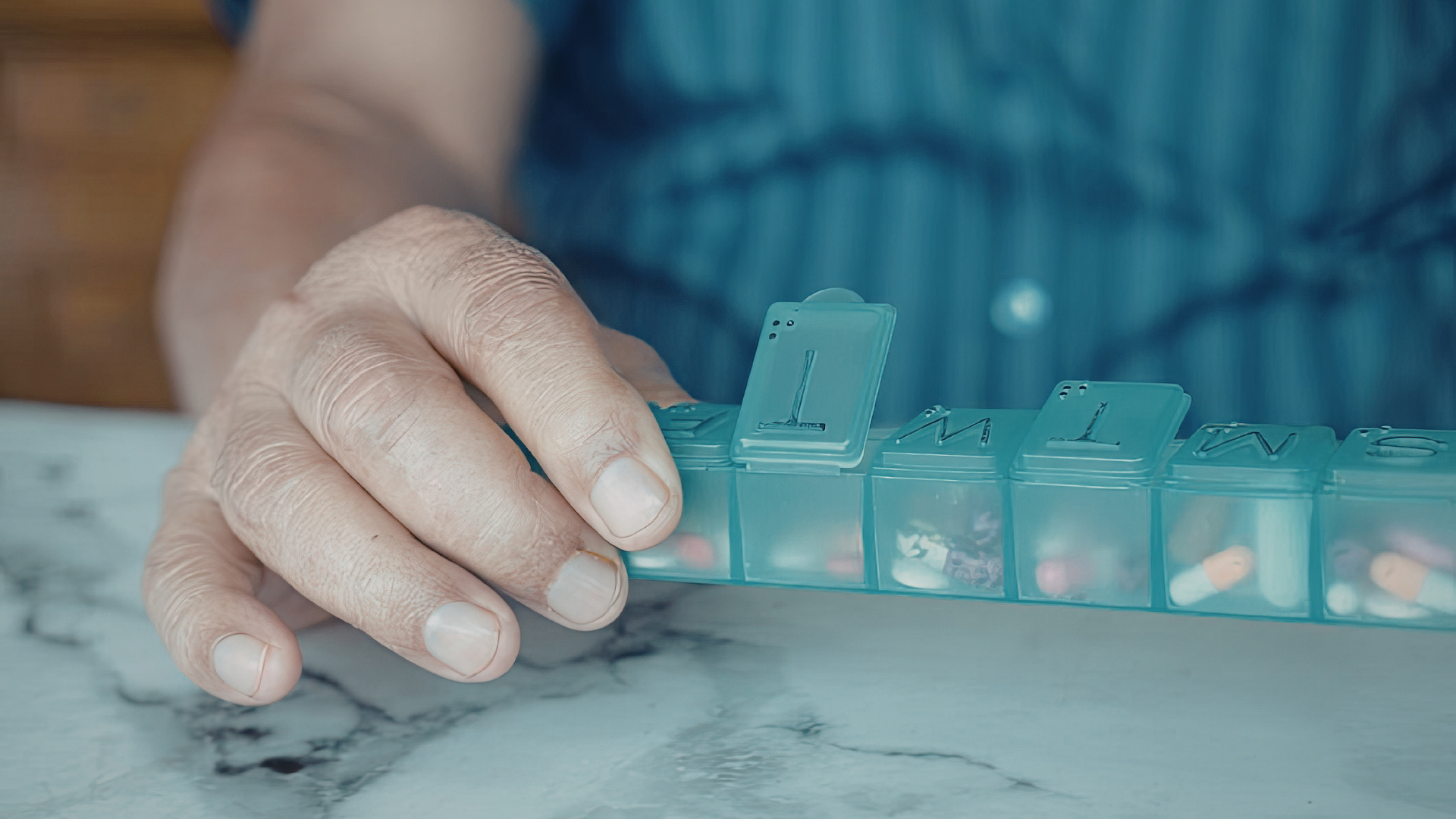 Hand placing a teal pill organizer on a marble table
