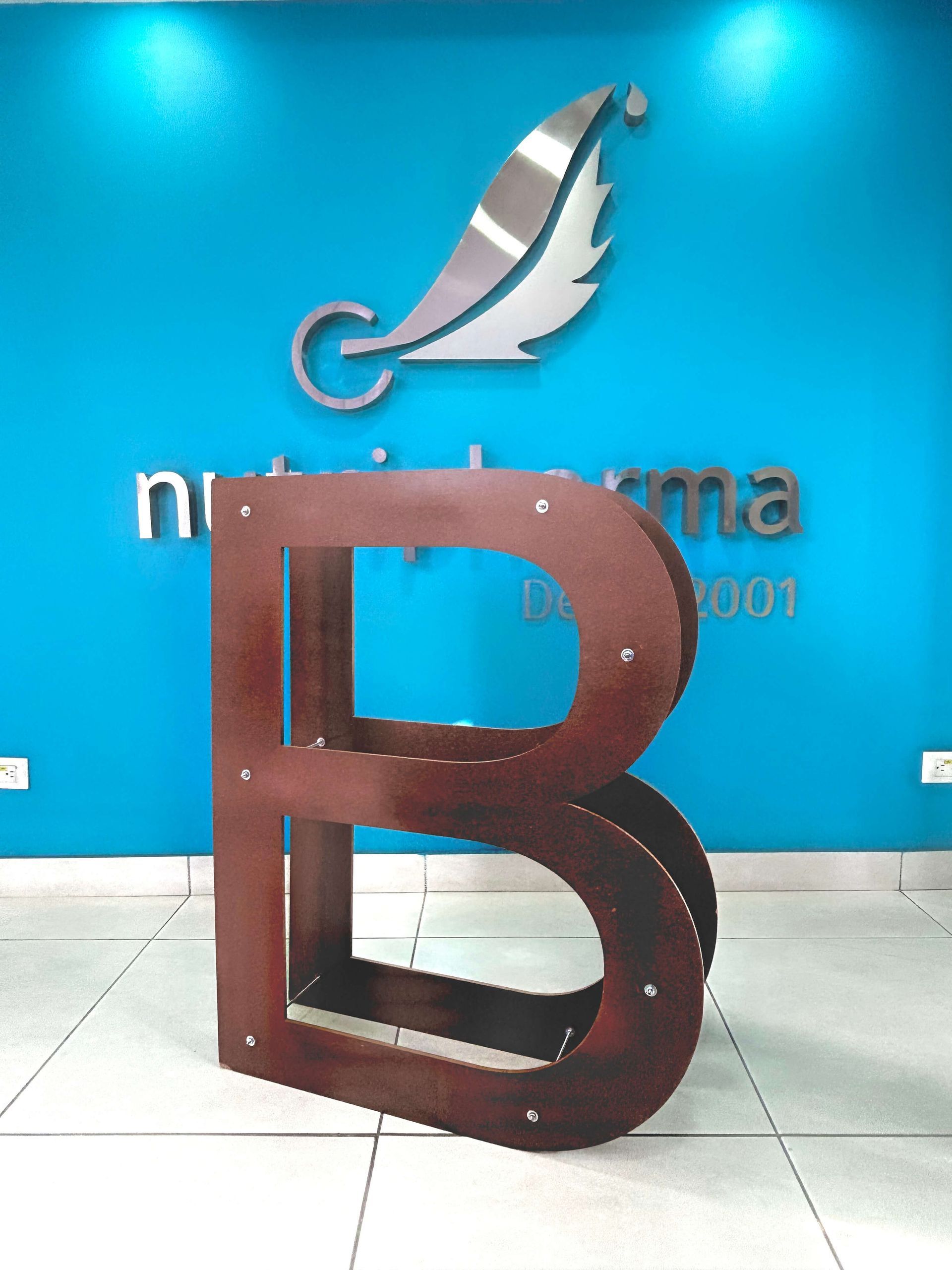 La B viajera frente al logo de Nutripharma, símbolo de Empresa B Certificada. B viajera a gran escala frente al logo de Laboratorios Nutripharma en sus instalaciones, símbolo del reconocimiento como Empresa B Certificada.
