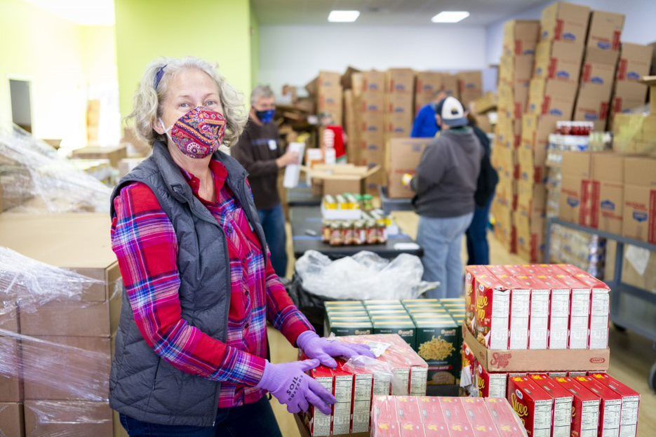 A woman wearing a mask and purple gloves is working in a warehouse.