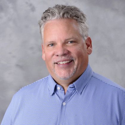 A man in a blue plaid shirt is smiling for the camera.