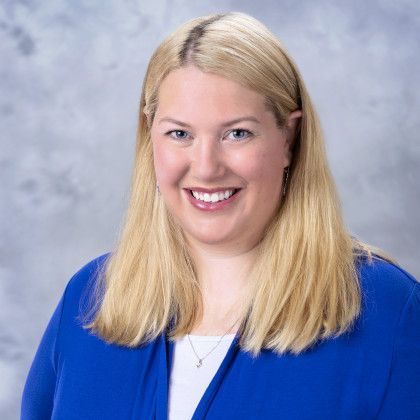 A woman is wearing a blue jacket and smiling for the camera.