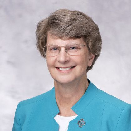 A woman wearing glasses and a blue jacket is smiling for the camera.