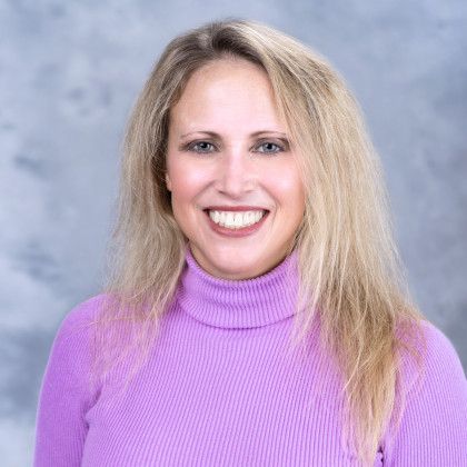 A woman in a purple sweater is smiling for the camera.