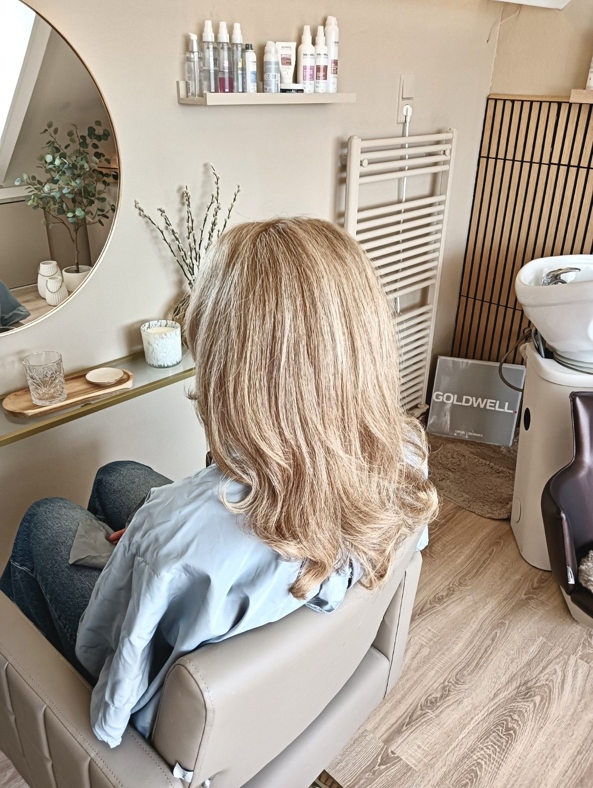 Persoon met krullend haar die in een kappersstoel voor een spiegel en wastafel zit