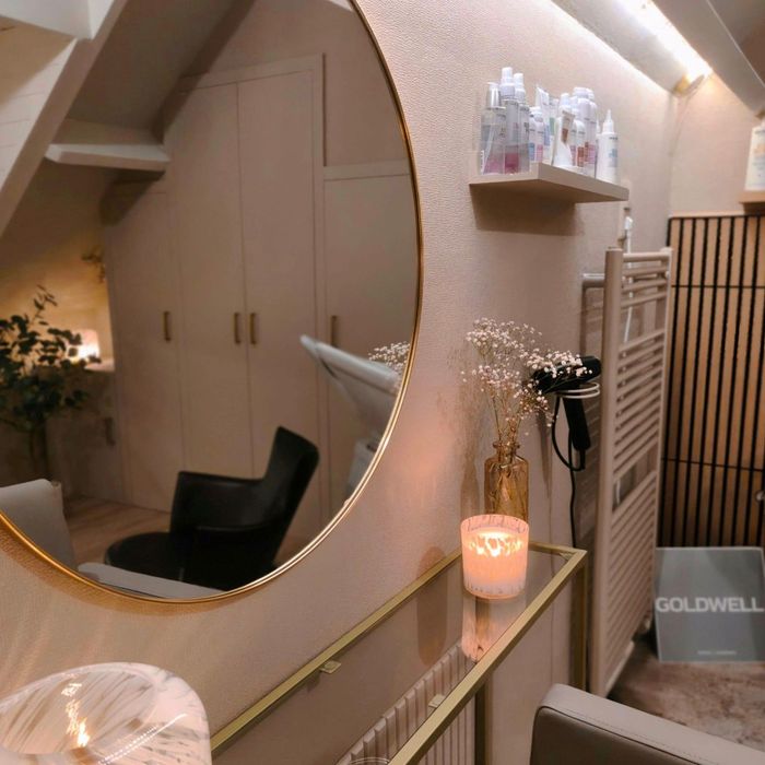 Kapsalon met ronde spiegel, warme verlichting, zwarte stoel, planken en haarproducten.