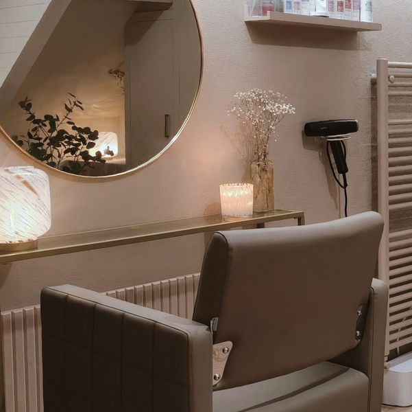 Knusse kappersstoel met spiegel, lamp, kaarsen en föhn in een warmbeige behandelkamer