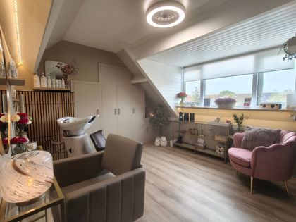 Lichte zolderkamer met roze fauteuil, grijze bank, hometrainer en groot raam met planten