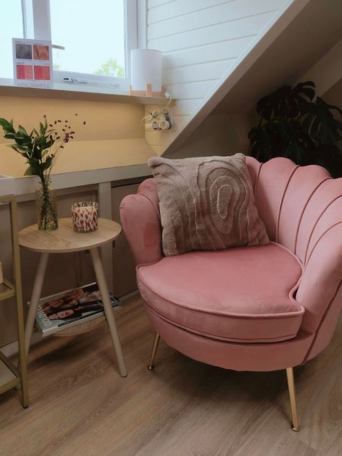 Roze fauteuil en bijzettafel in een knus hoekje op zolder, met planten en een raam.