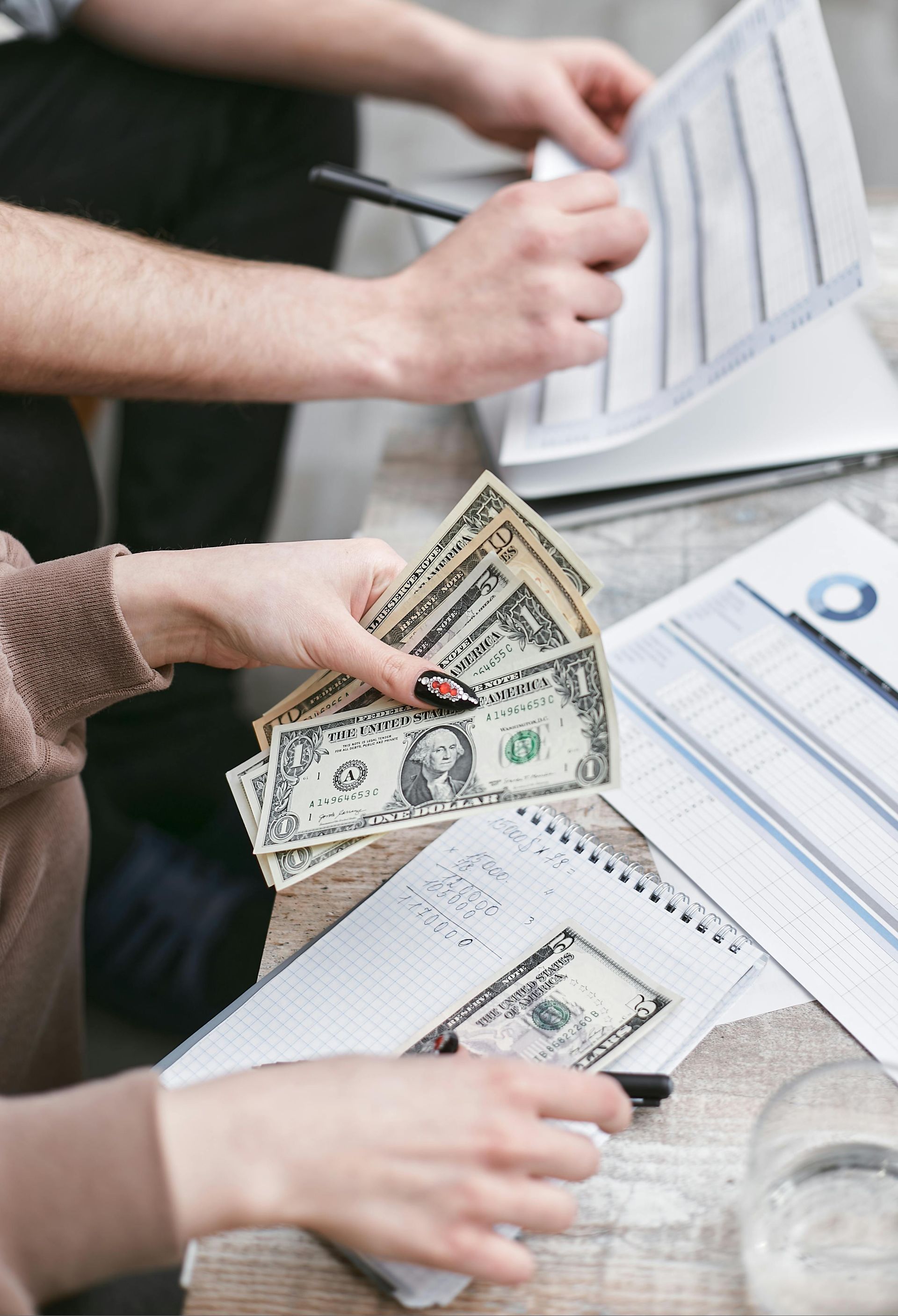 Hands holding cash, working on paperwork with another person; finances.