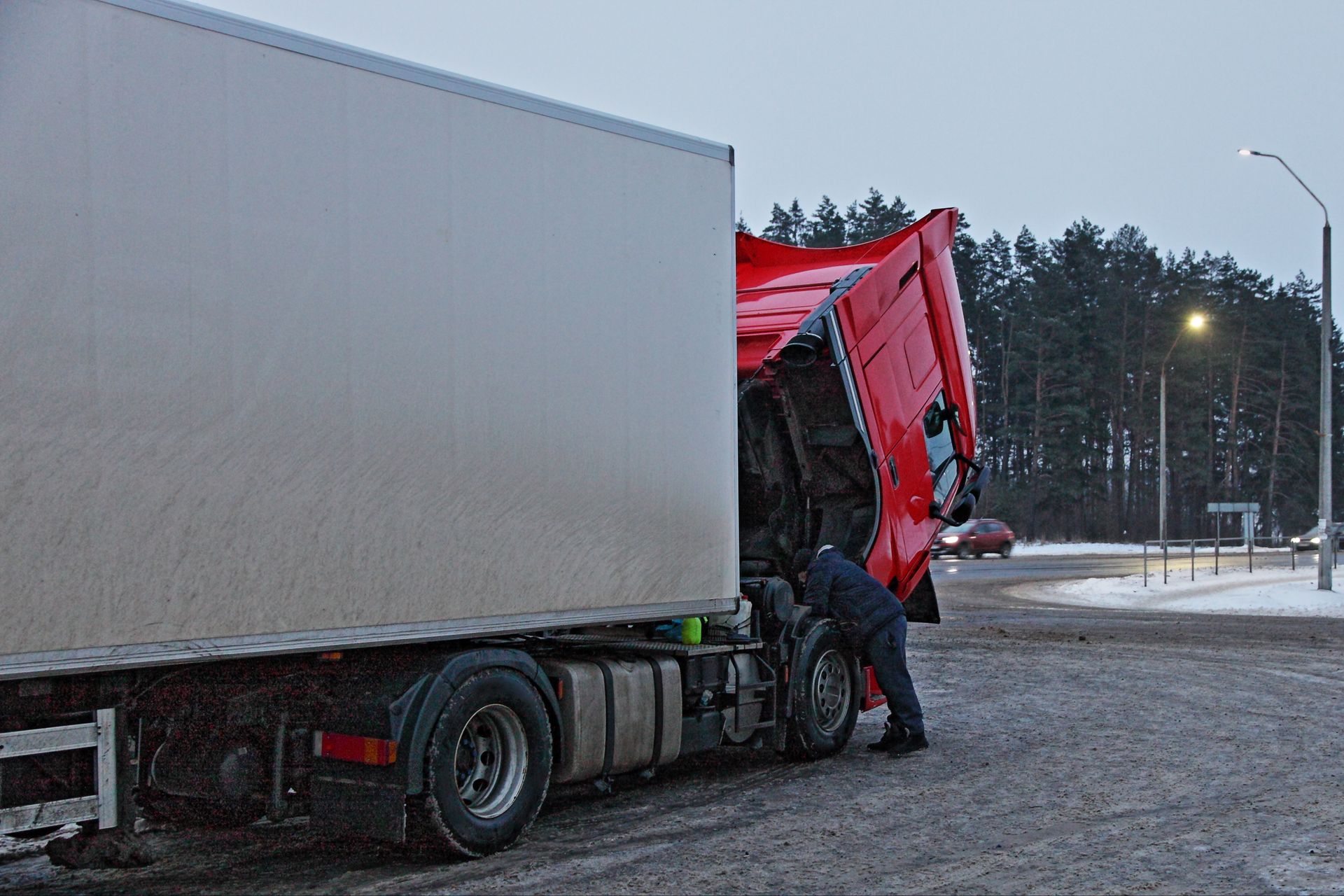 Professional auto mechanic choosing right wrench. Heavy red semi-truck with trailer diesel engine repair under opened cab hood at cold winter snowy road.