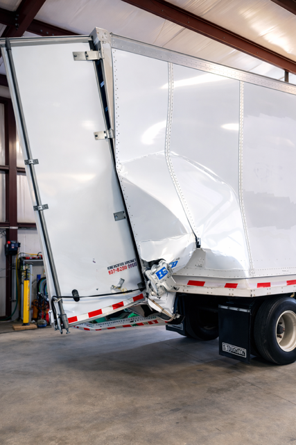 Two white box trucks with rear ends crushed together inside a warehouse