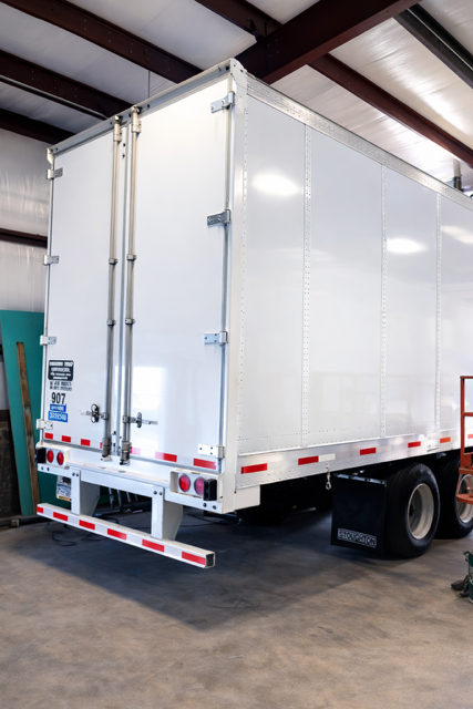 White box truck parked inside a warehouse, rear doors facing the camera.