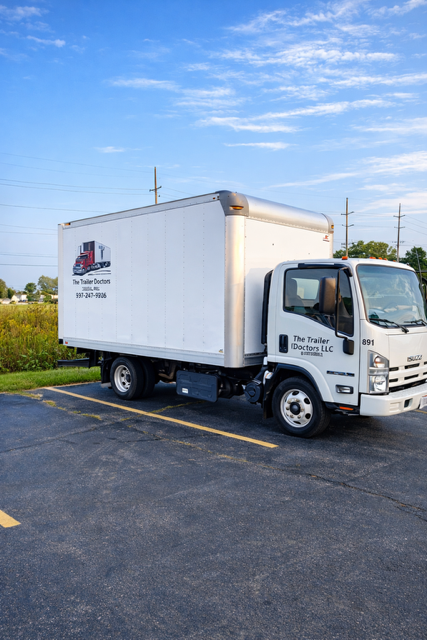 White box truck parked on asphalt under a blue sky, with logo on the side.