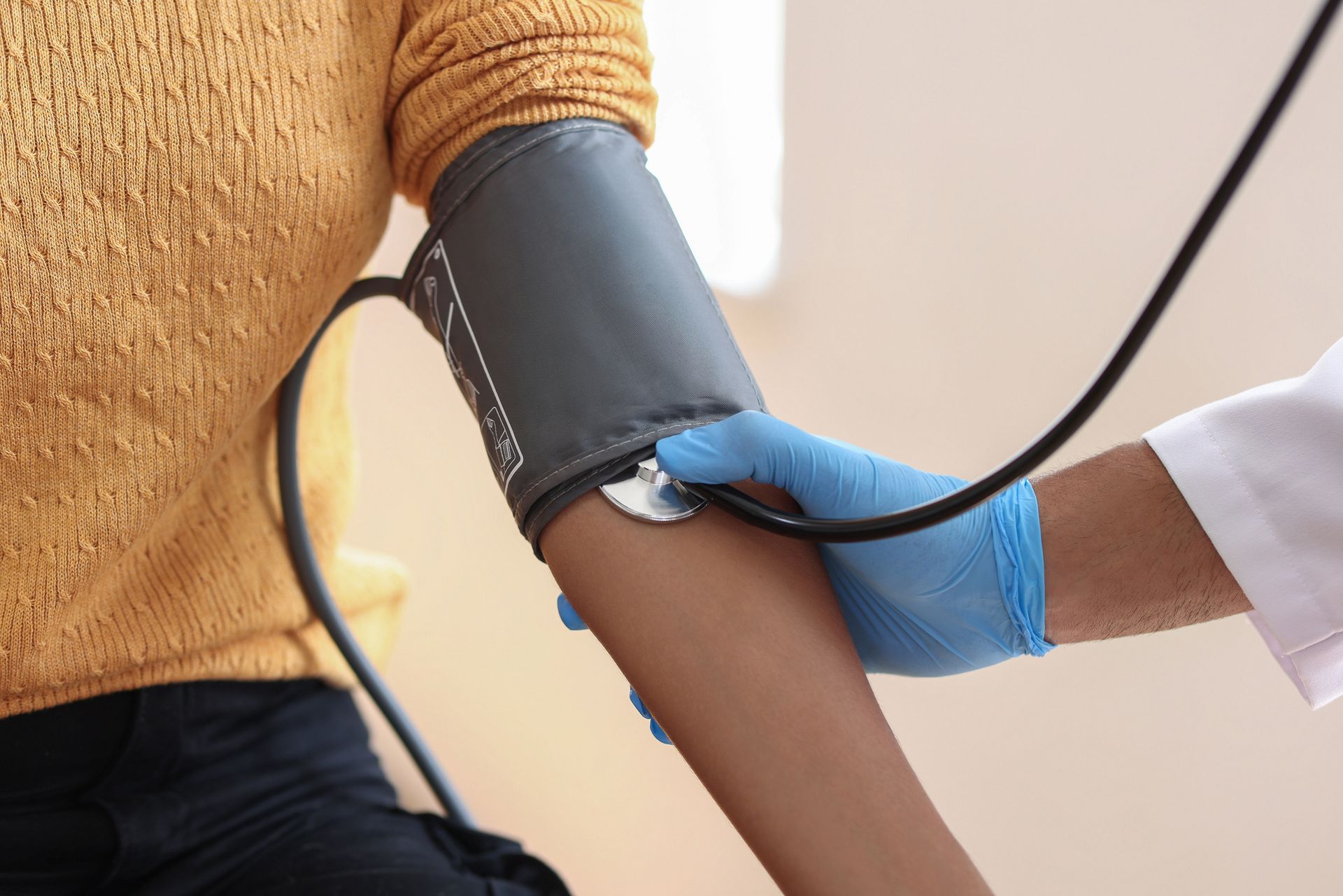 Person's arm in a blood pressure cuff, being checked by a gloved healthcare worker.