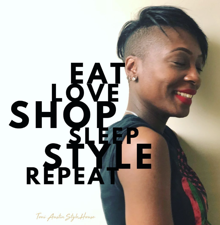 A woman with a shaved head is smiling in front of a sign that says eat love shop sleep style repeat