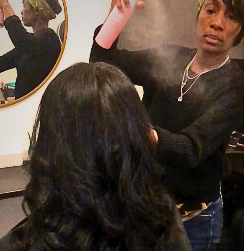 A woman spraying a woman 's hair in front of a mirror