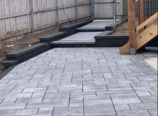 Grey stone patio and steps leading up to a wooden deck, next to a wooden fence.