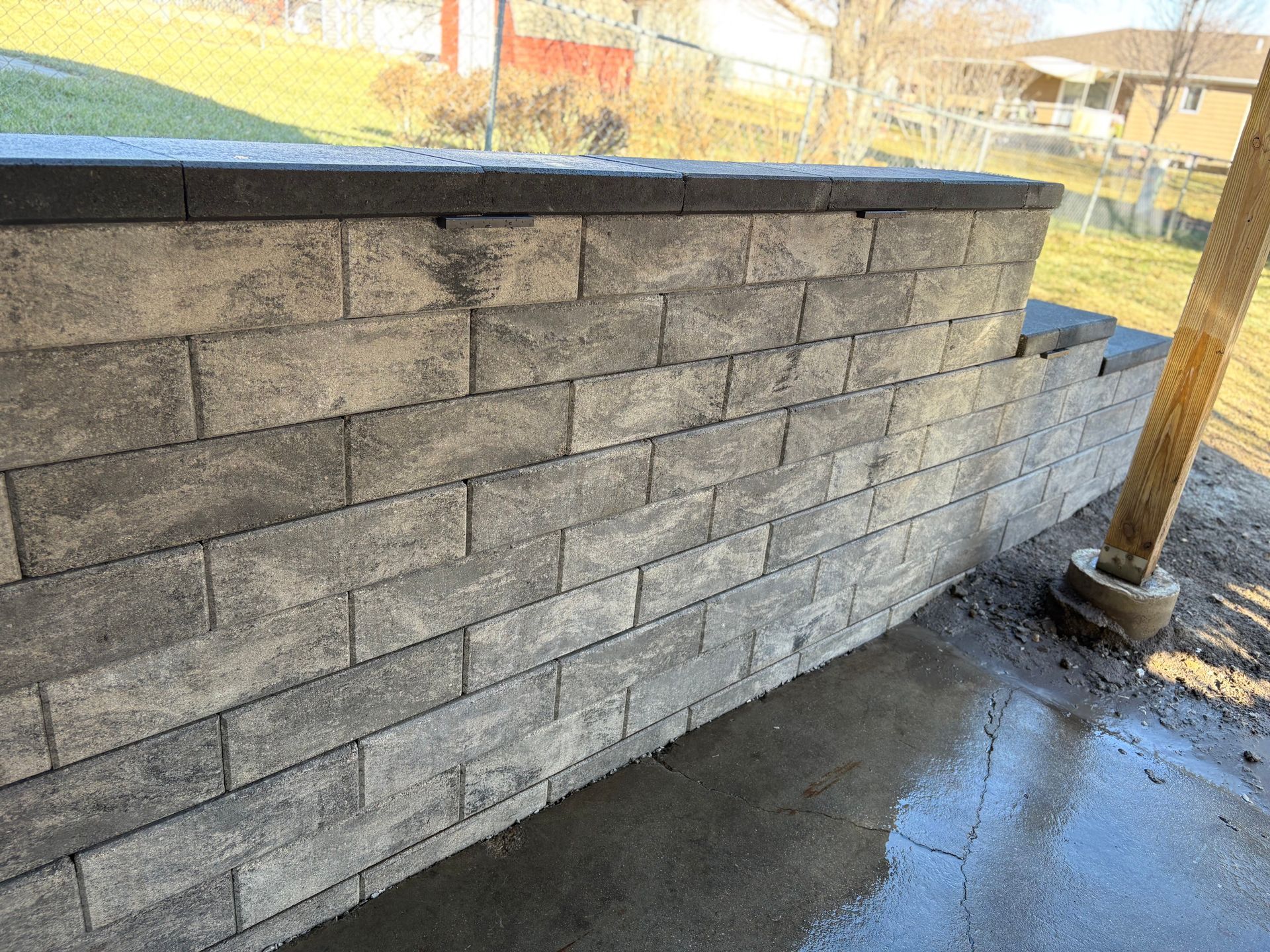 Gray brick retaining wall. Top row is dark gray. Concrete pillar on right.