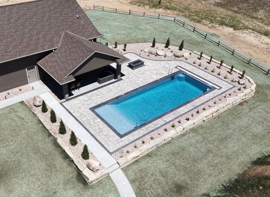 Aerial view of a house with a fenced backyard and a rectangular blue swimming pool surrounded by patio stones.