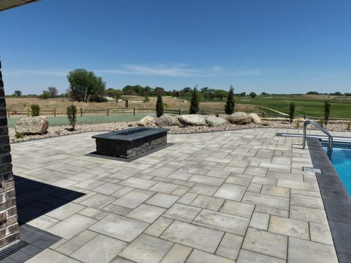 Gray brick patio with steps leading up, next to wooden deck and fence.