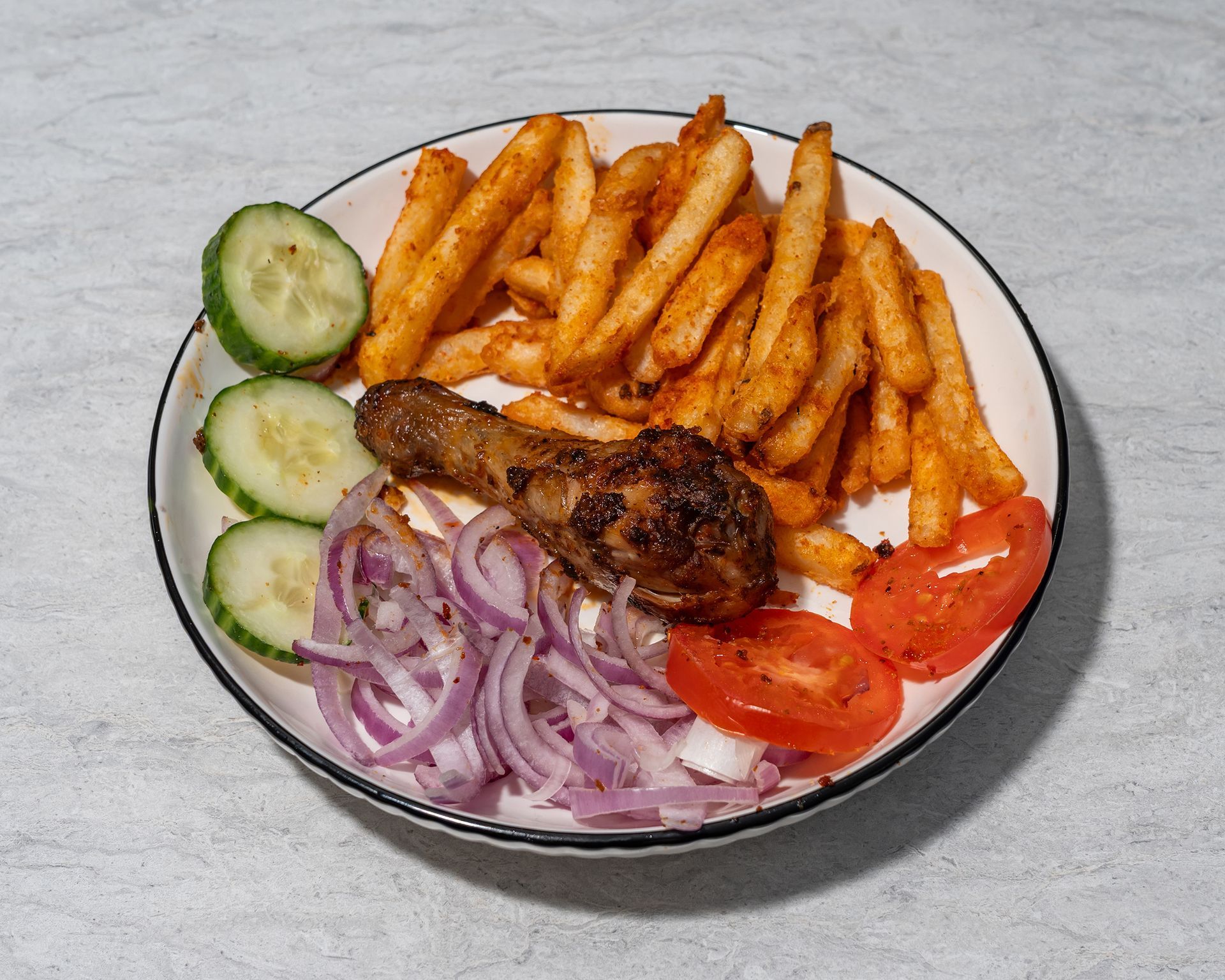 Grilled chicken with fries, cucumber slices, onion rings, and tomato wedges on a white plate