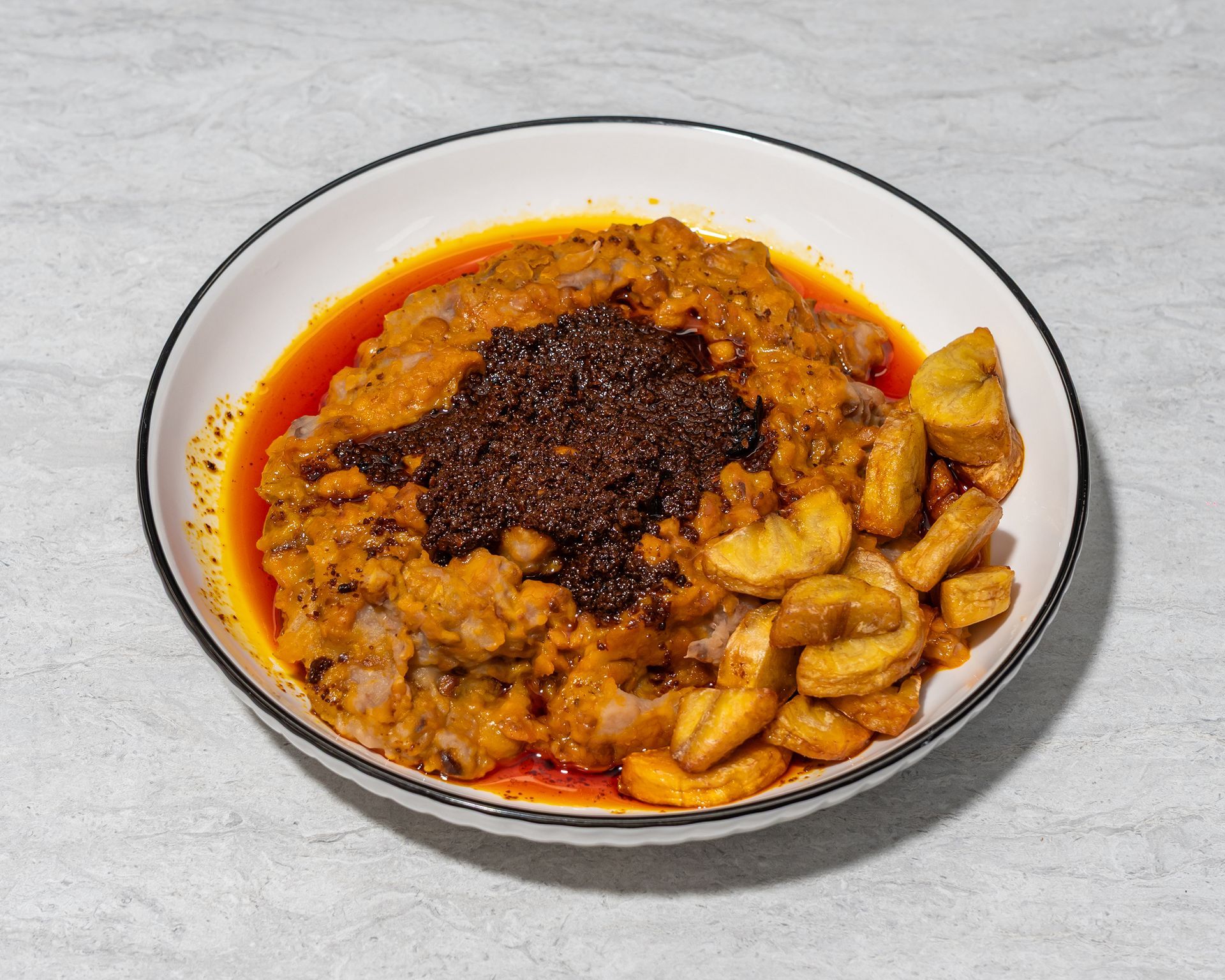 Bowl of orange stew with chunks and dark chili oil in the center