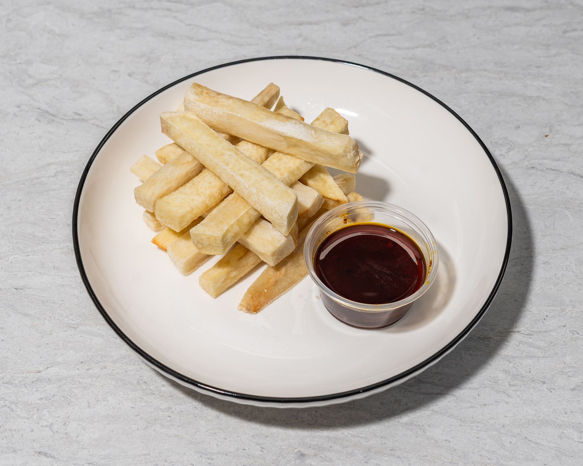 Plate of French fries with a small cup of red dipping sauce on a gray surface