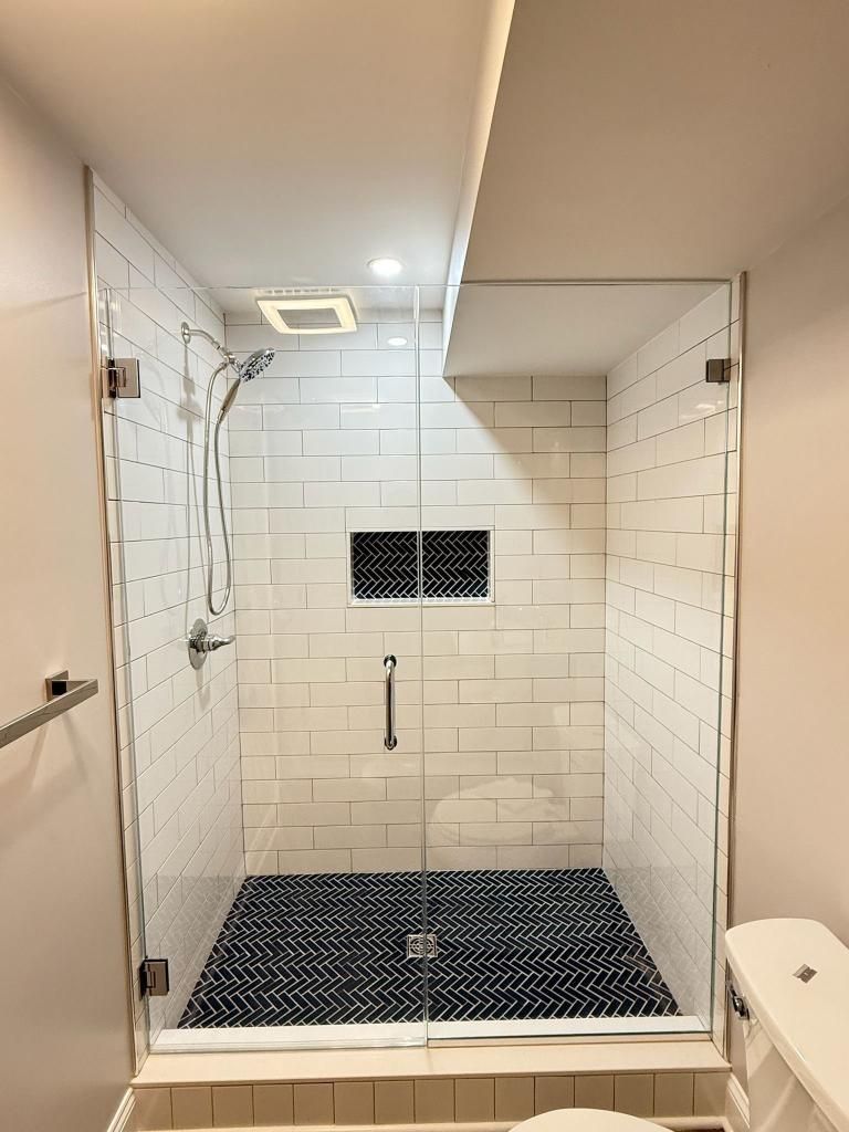Walk-in shower with white subway tile, black floor tiles, and wall-mounted handheld showerhead