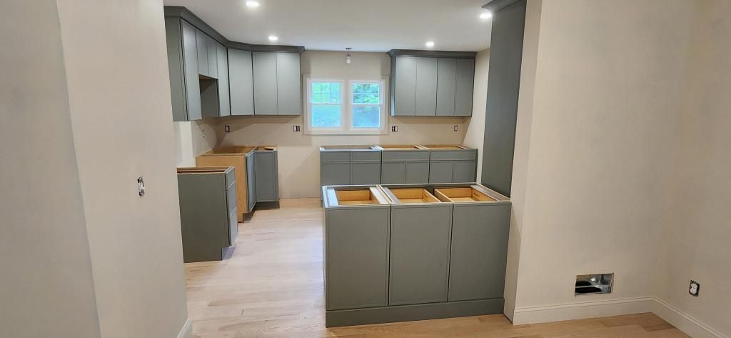 Empty modern kitchen and dining area with light wood floors, gray cabinets, and a windowed back wall