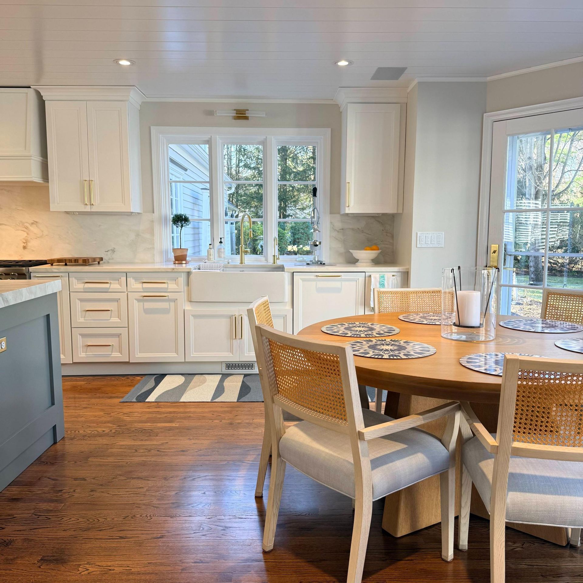 Bright kitchen with white cabinets, wood floors, and a round dining table by windows.