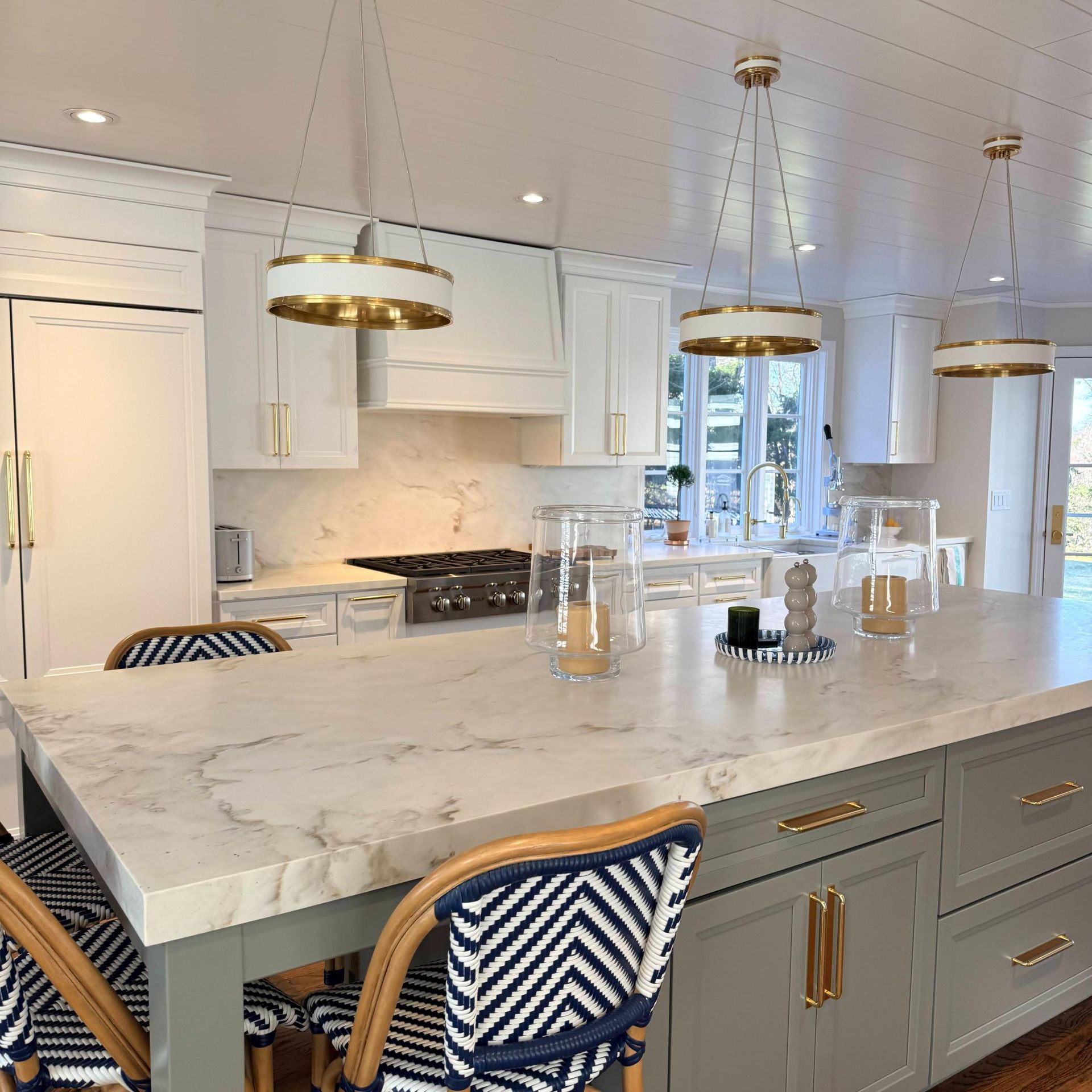 Bright white kitchen with marble island, brass pendant lights, and upholstered bar stools