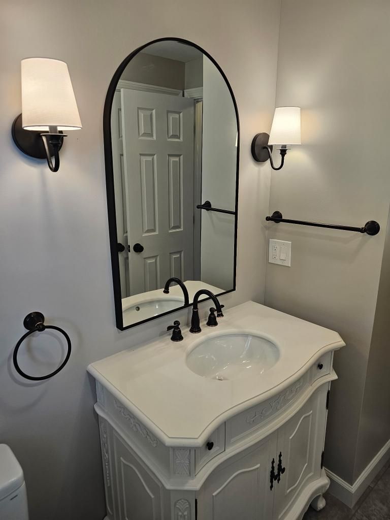 Bathroom vanity with oval mirror, white sink cabinet, and wall sconces on light gray walls