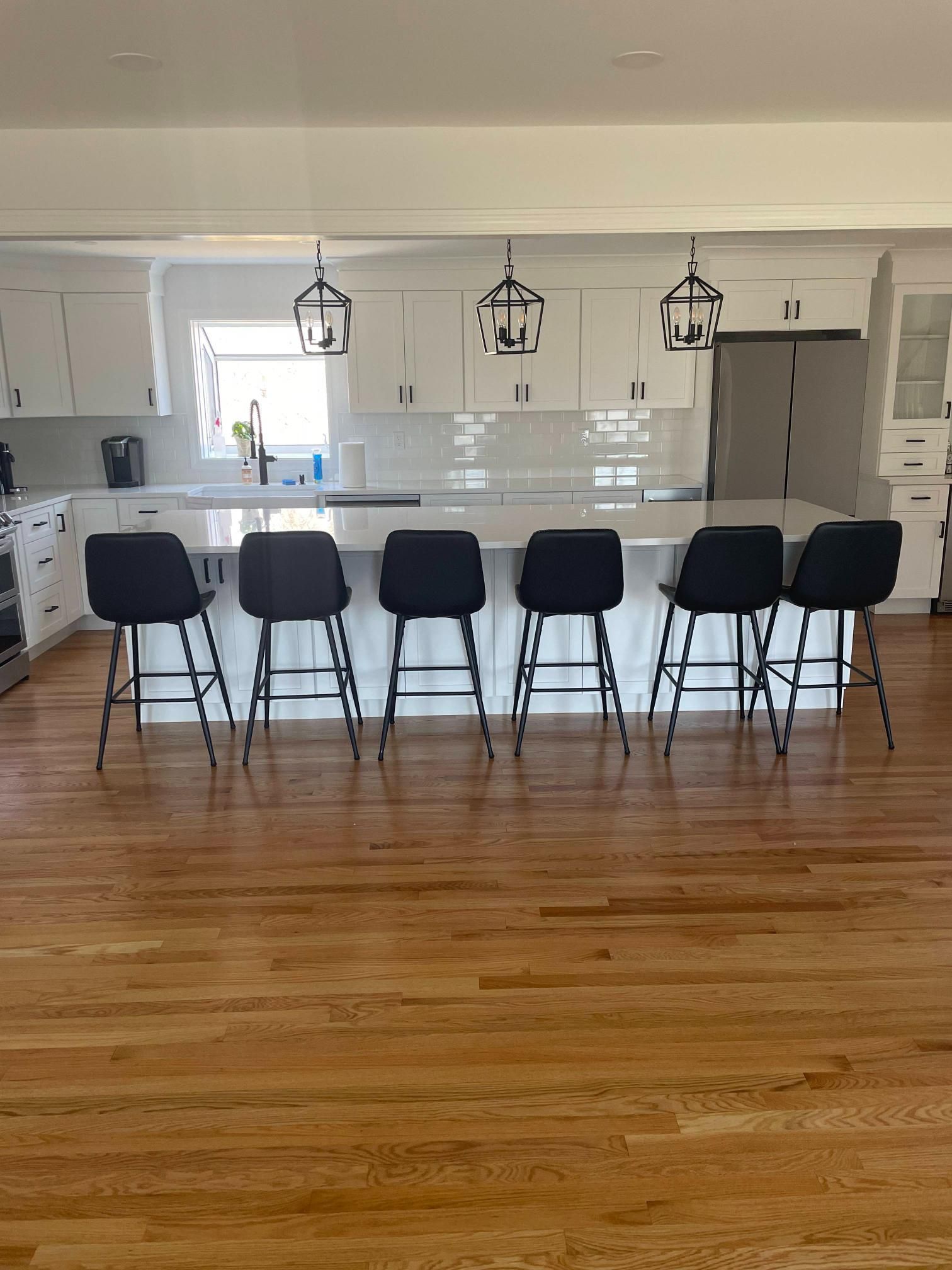 Modern kitchen with white cabinets, island, six black bar stools, and hardwood floors