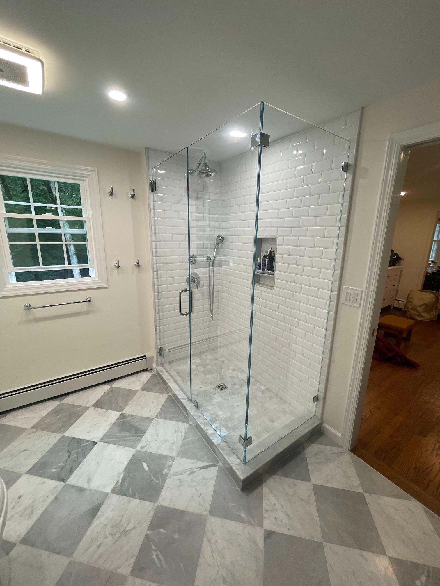 Modern bathroom with glass shower enclosure, white subway tile, and gray diamond-pattern floor tiles.
