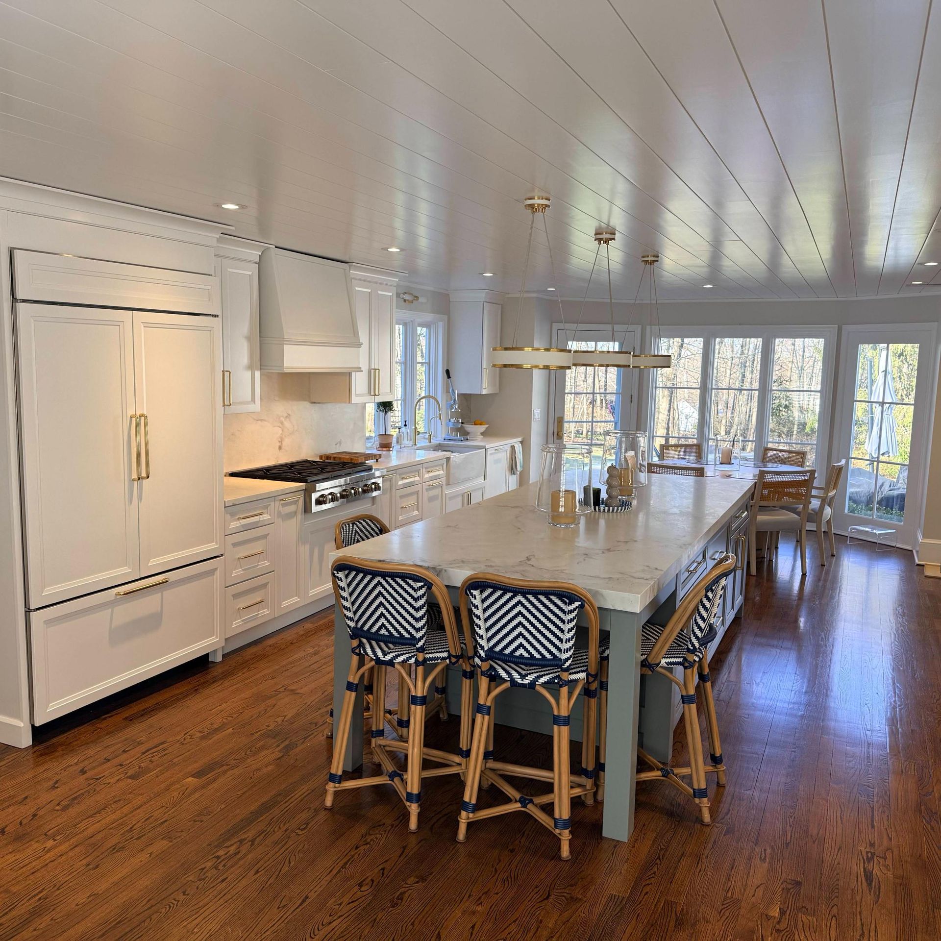 Bright open kitchen with white cabinets, island seating, hardwood floors, and large windows overlooking water