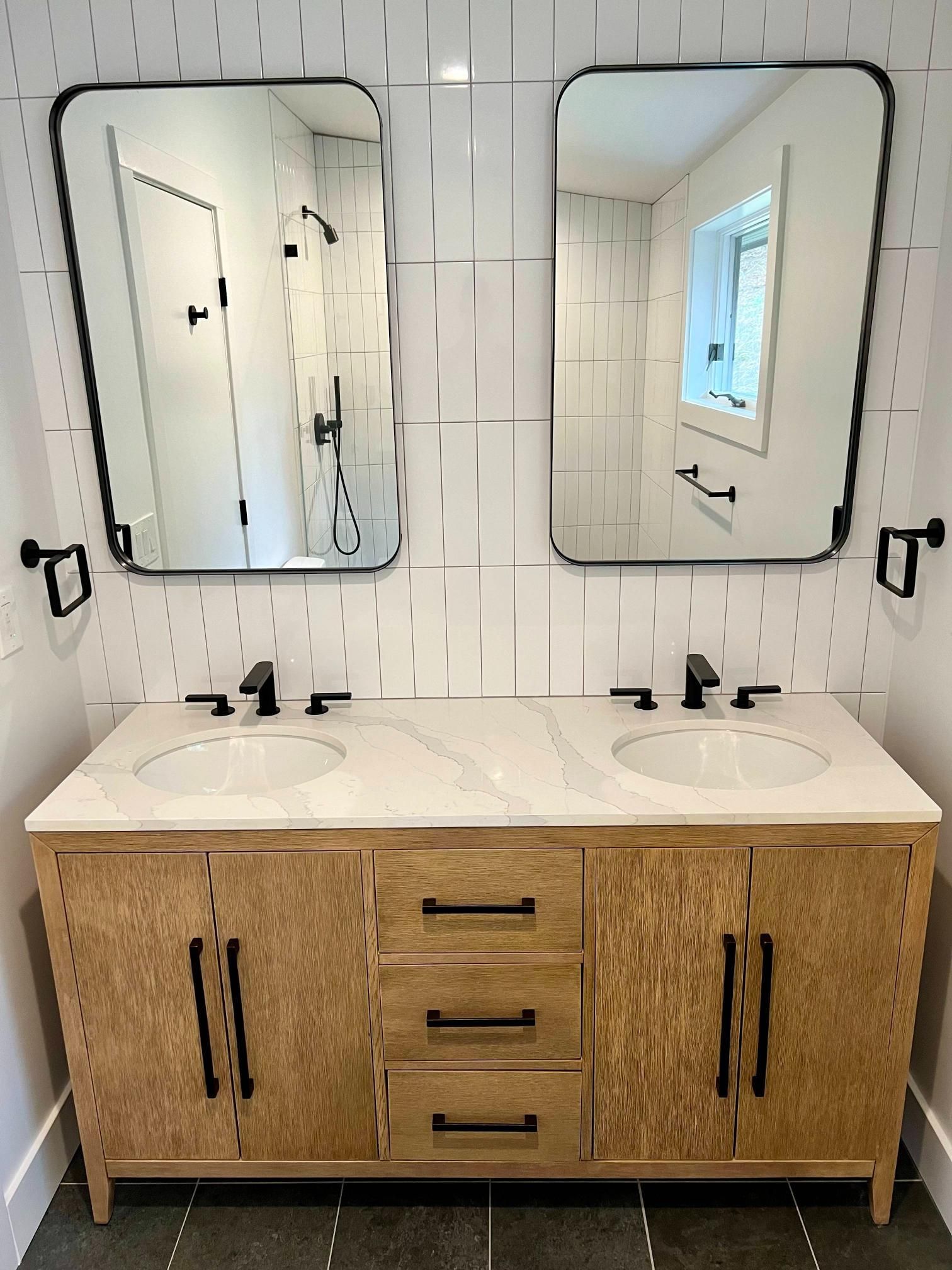 Double vanity bathroom sink with wood cabinets and two mirrors in a bright tiled room