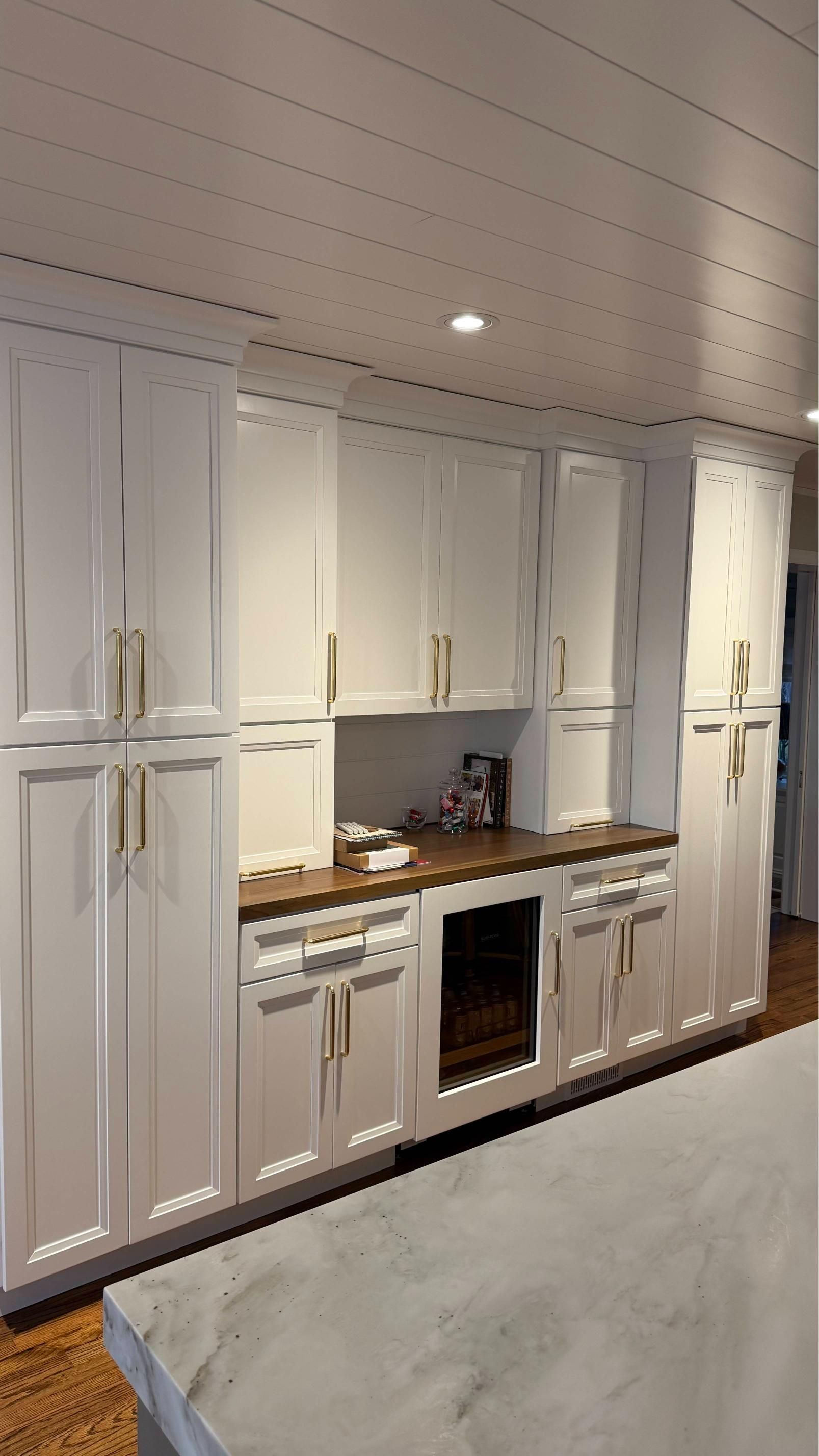 Built-in white kitchen cabinets and stove beneath a wood-paneled ceiling