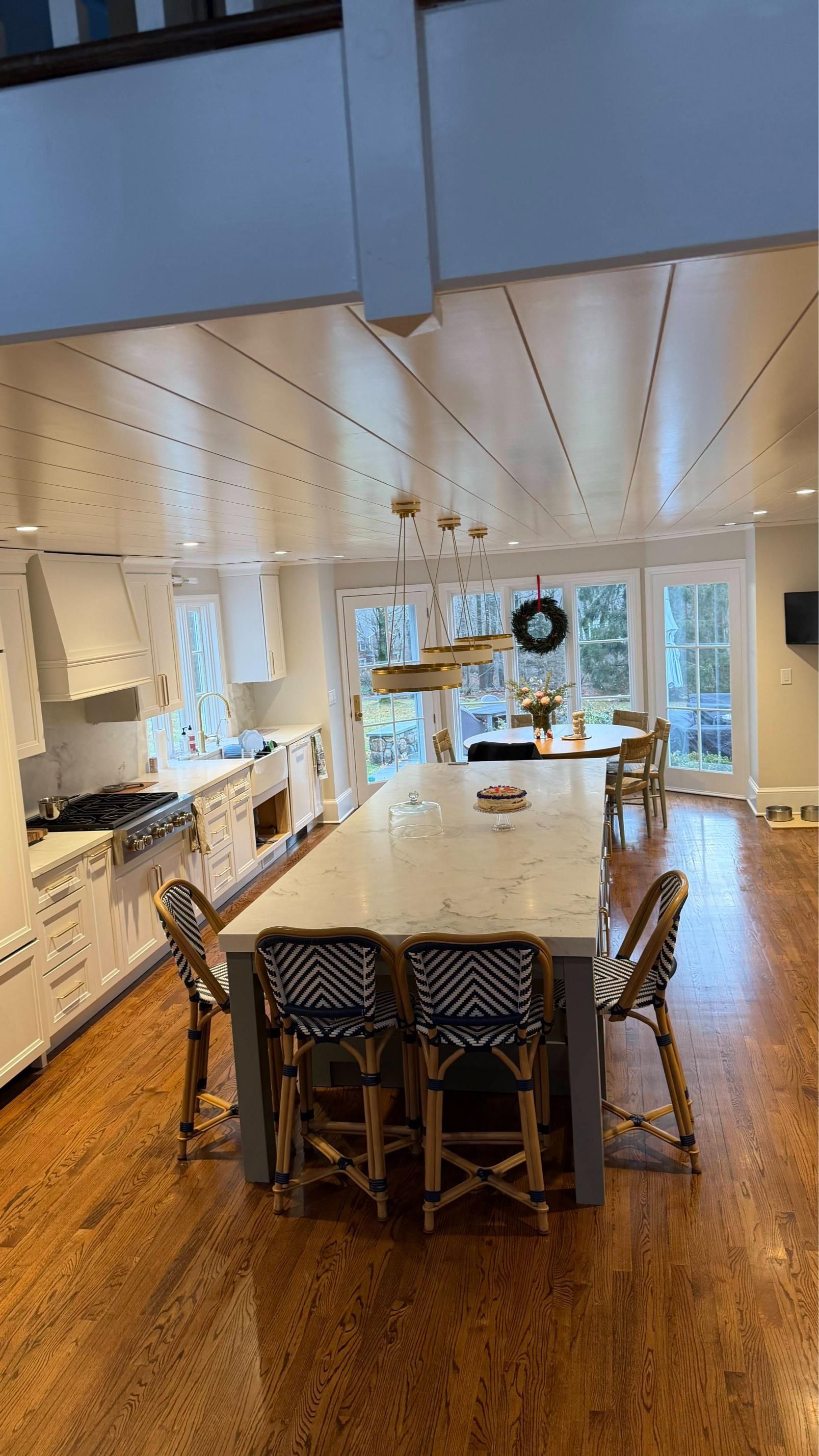 Bright kitchen with island, wooden stools, white cabinets, and large windows overlooking a dining area.