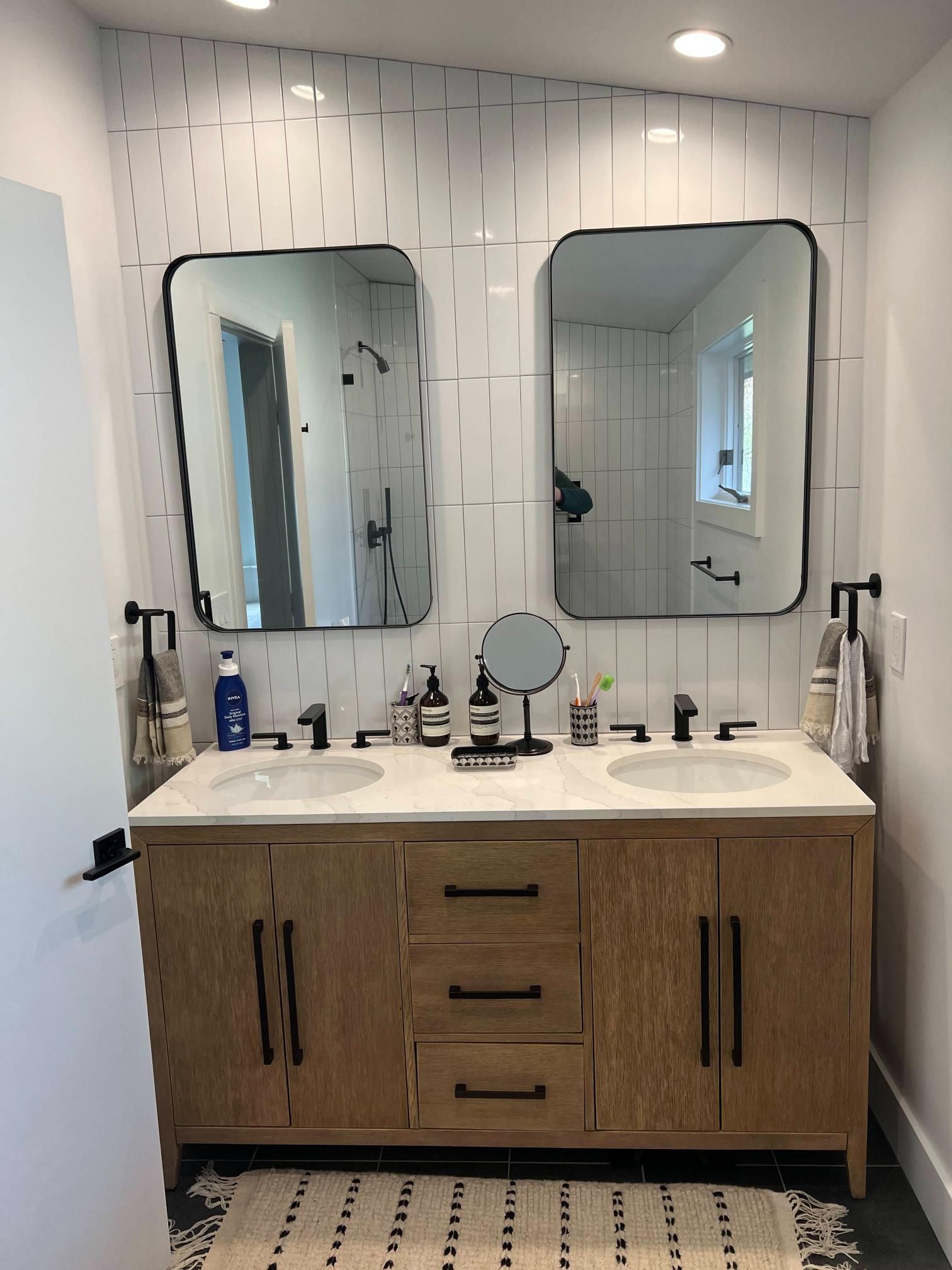 Modern bathroom vanity with double mirrors, white tile walls, and wood cabinets
