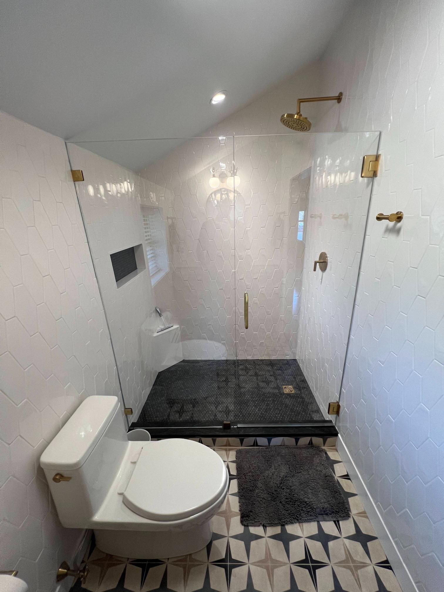 Small white bathroom with toilet, shower bench, grab bars, and black-and-white tile floor