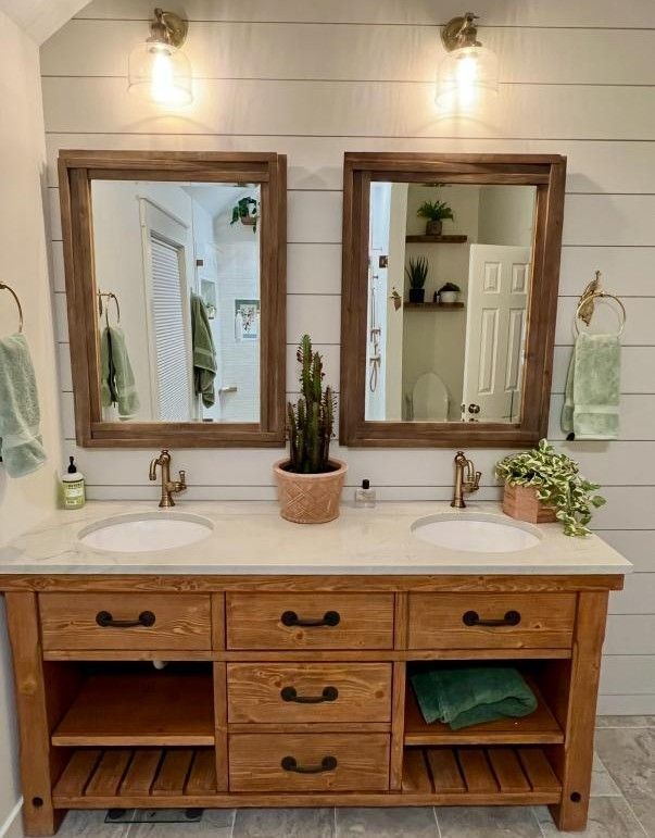 Rustic wood vanity with double mirrors, white countertop, sconces, and potted plants in a bathroom