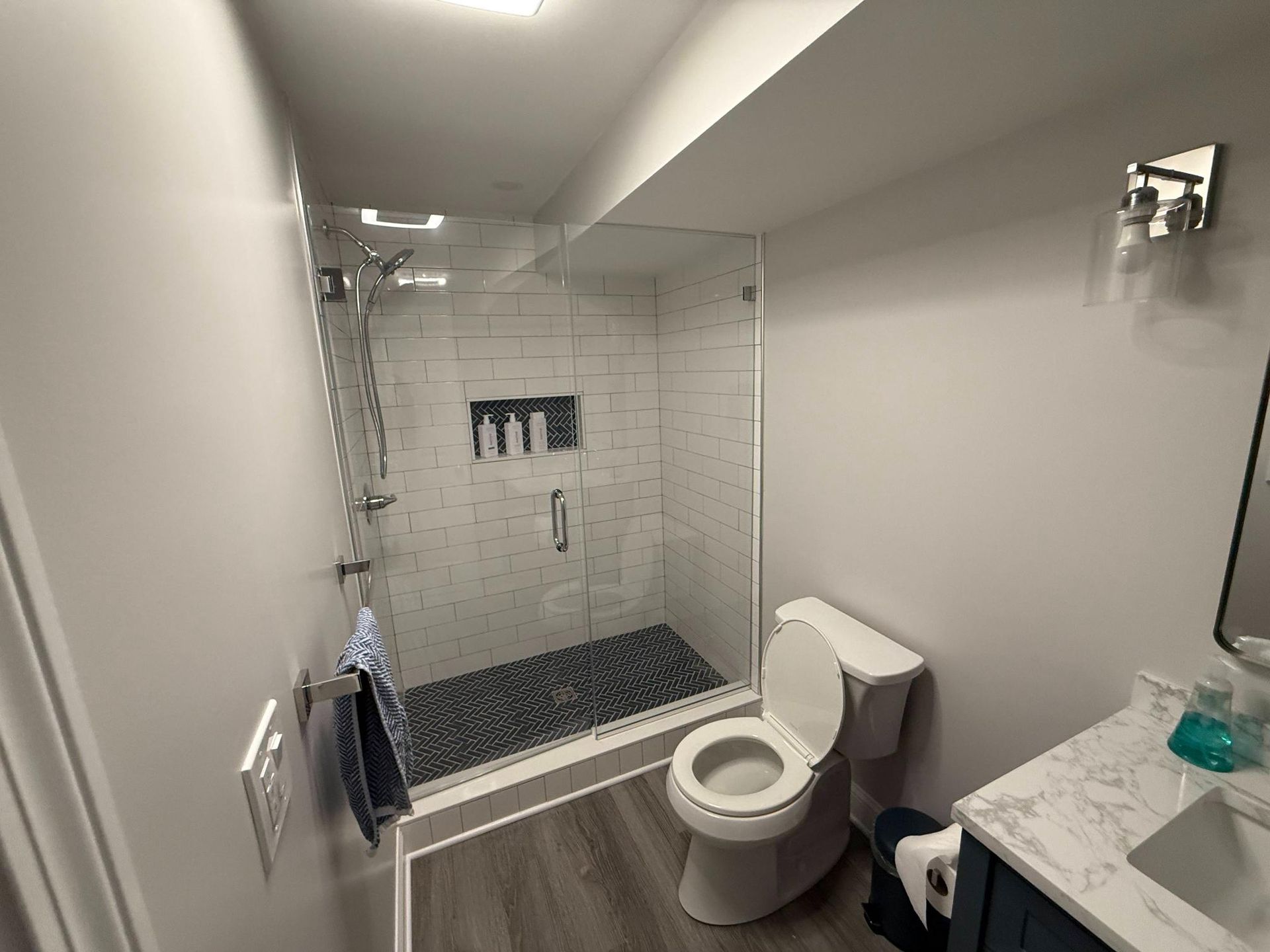 Modern white bathroom with walk-in shower, toilet, and marble vanity countertop