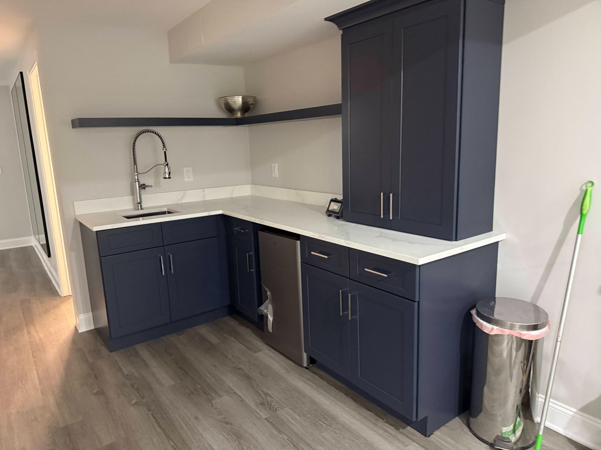 Modern kitchen corner with navy cabinets, white countertop, sink, and wood-look flooring.