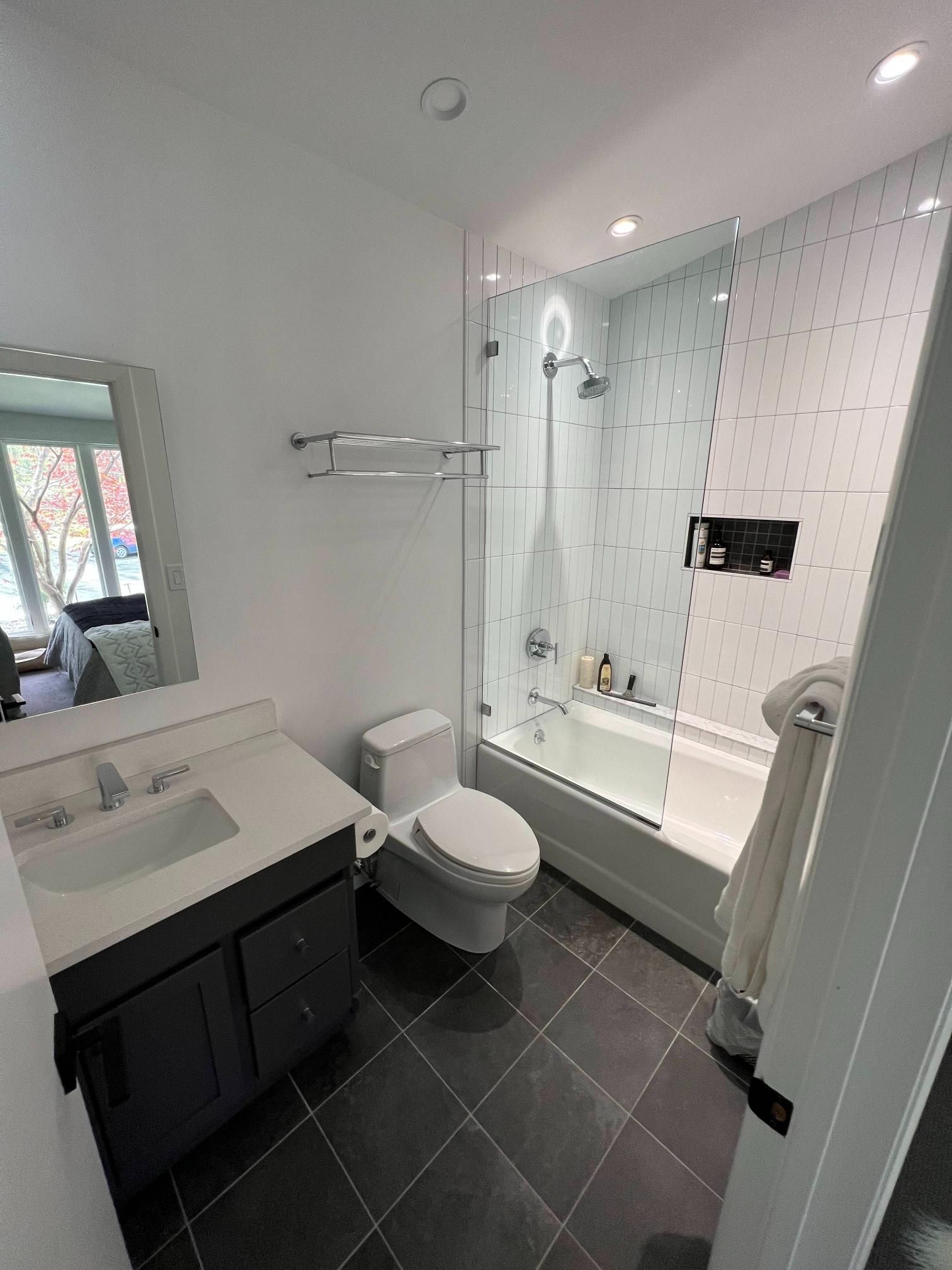 Modern bathroom with vanity, toilet, and glass-enclosed bathtub shower in white and gray.