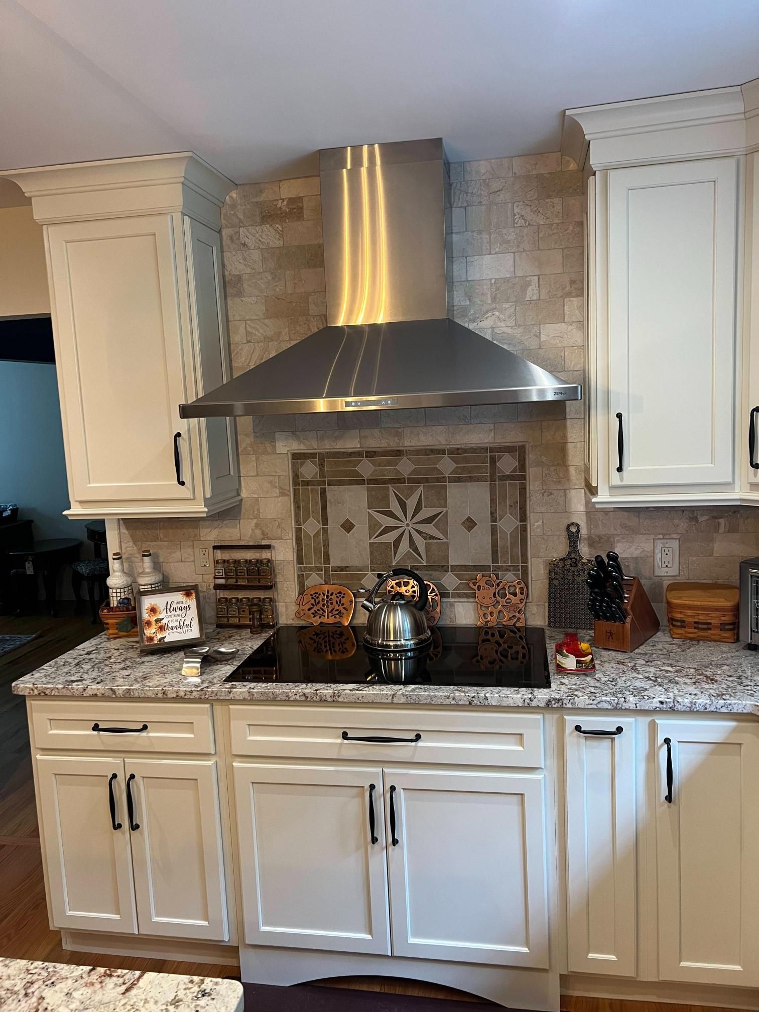 Kitchen with white cabinets, stainless range hood, tiled backsplash, and granite countertops.