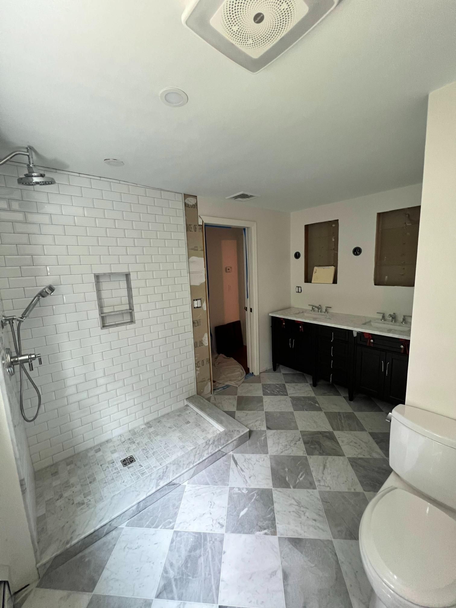 Small bathroom with tiled shower, vanity, and toilet; gray-and-white floor and white subway tile walls