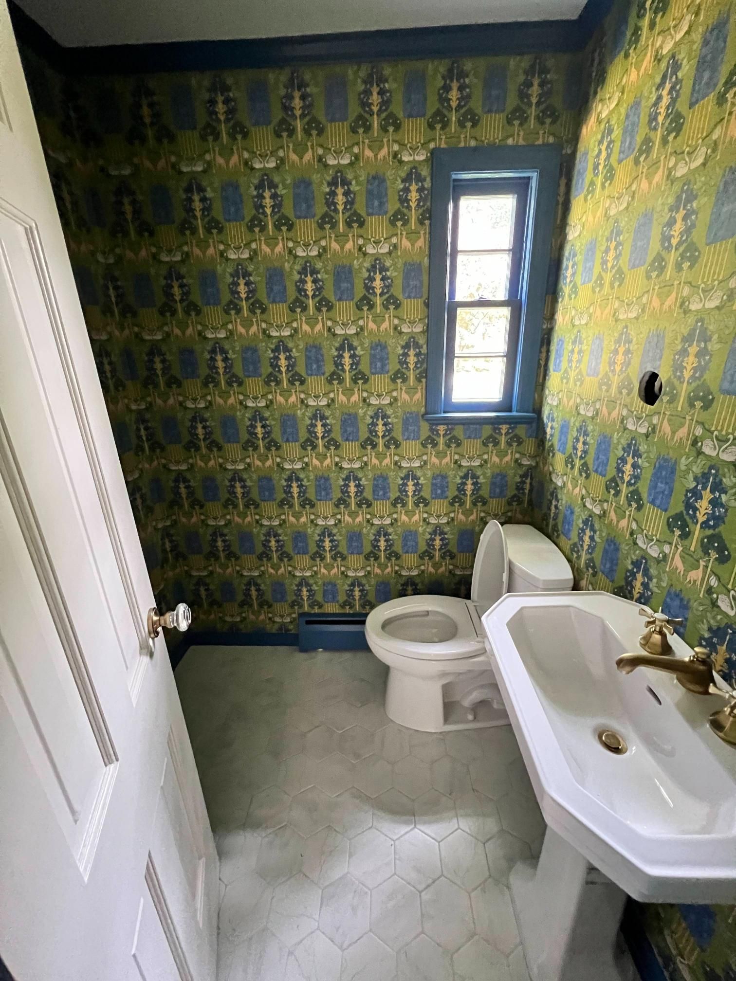 Small bathroom with green patterned wallpaper, toilet, sink, and narrow window.